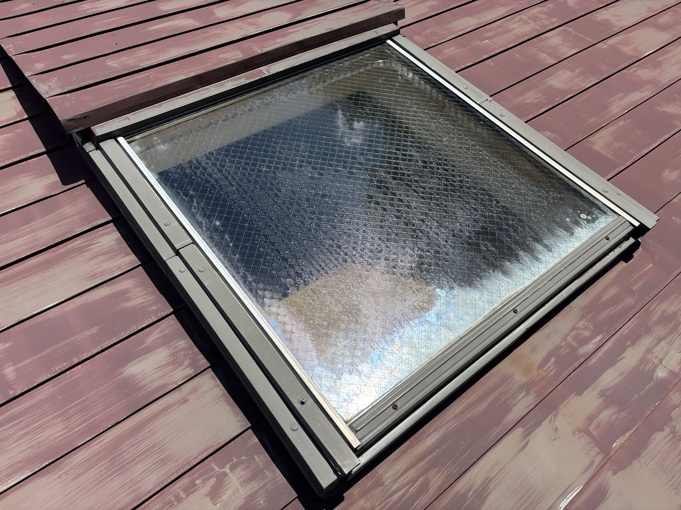 雨漏りしたVELUX(ベルックス)の天窓を、屋根の上から斜めに見たところ。網入りガラスの下側に、白い水あかの跡がある